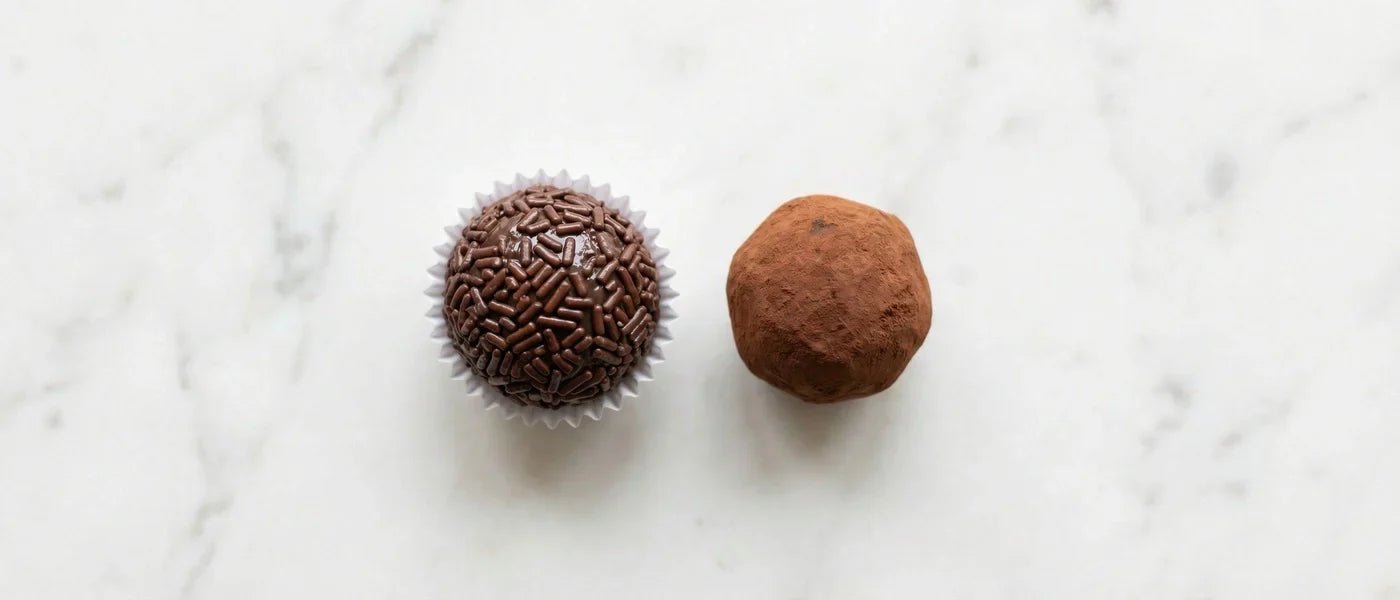 Side by side comparison of a Brazilian brigadeiro and a chocolate truffle on white marble surface — texture and coating differences