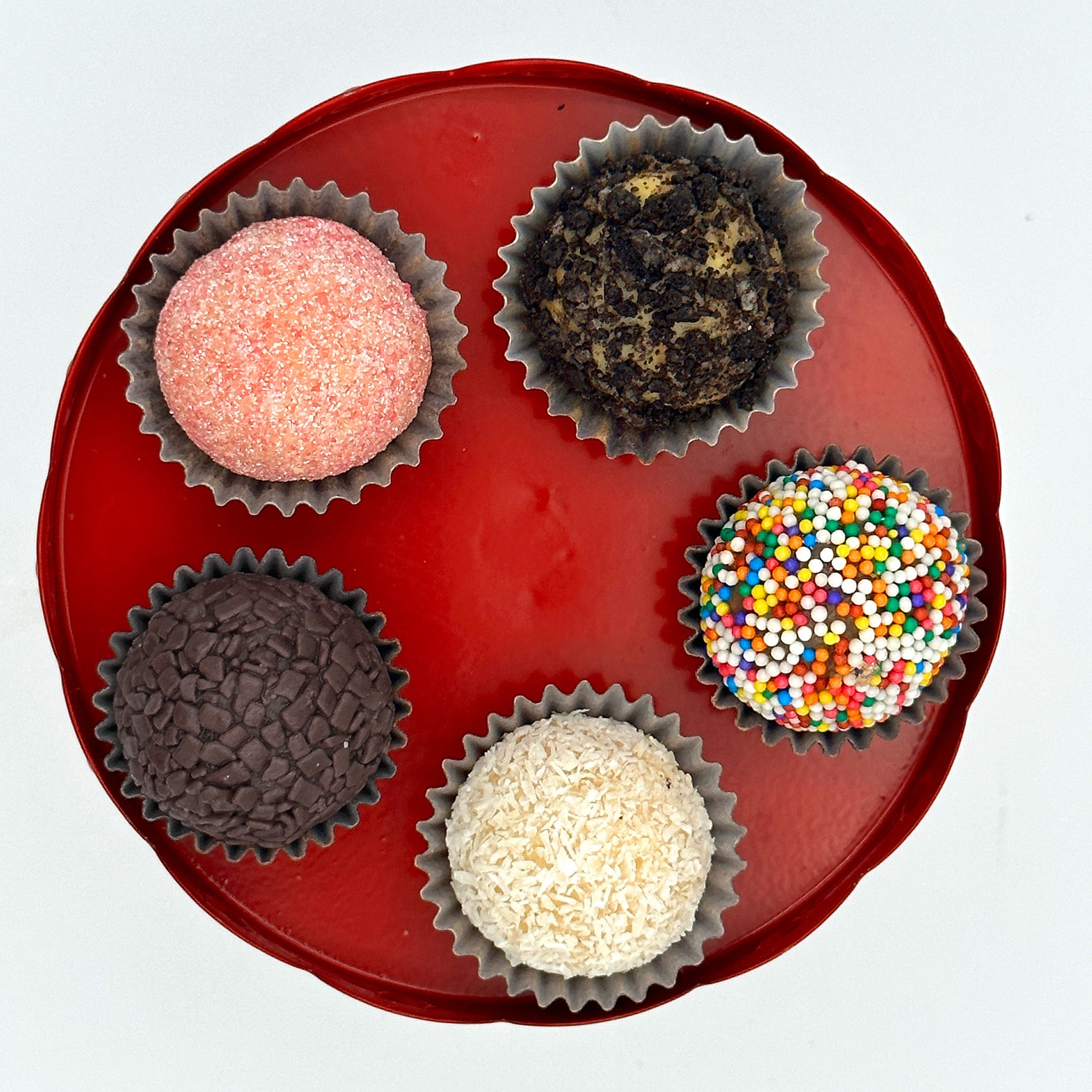 Five colorful sprinkled Anniversary Classic Celebration Brigadeiros in a red tin on a white background.